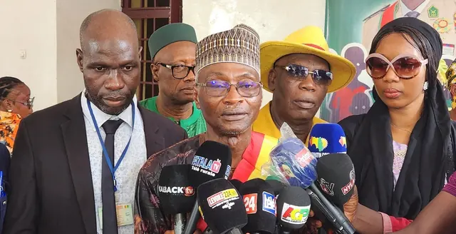 M. Aboubacar Molota Camara, au centre, avec une coiffe et une écharpe aux couleurs de la Guinée, face aux microphones.